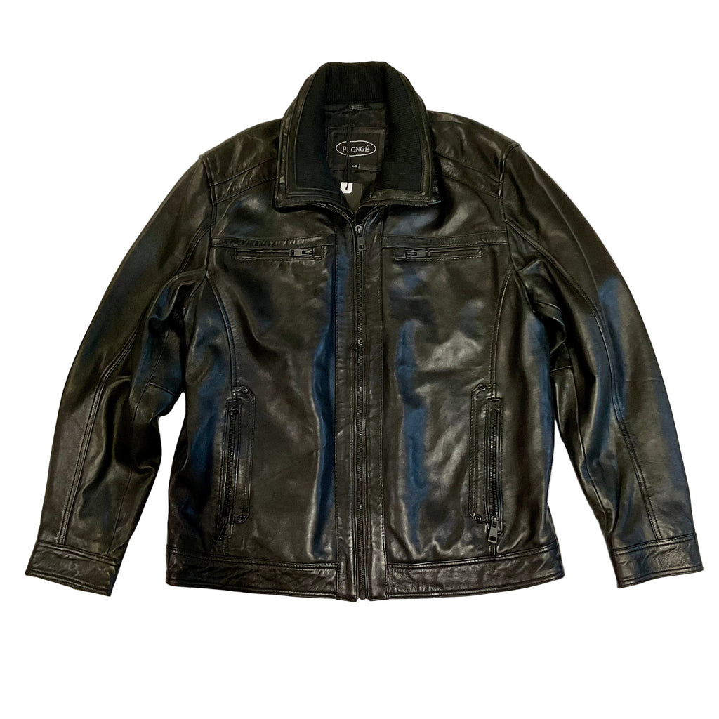 A black leather men's jacket with a standing collar, zippered front, and zippered chest pockets, displayed against a brick wall background.
